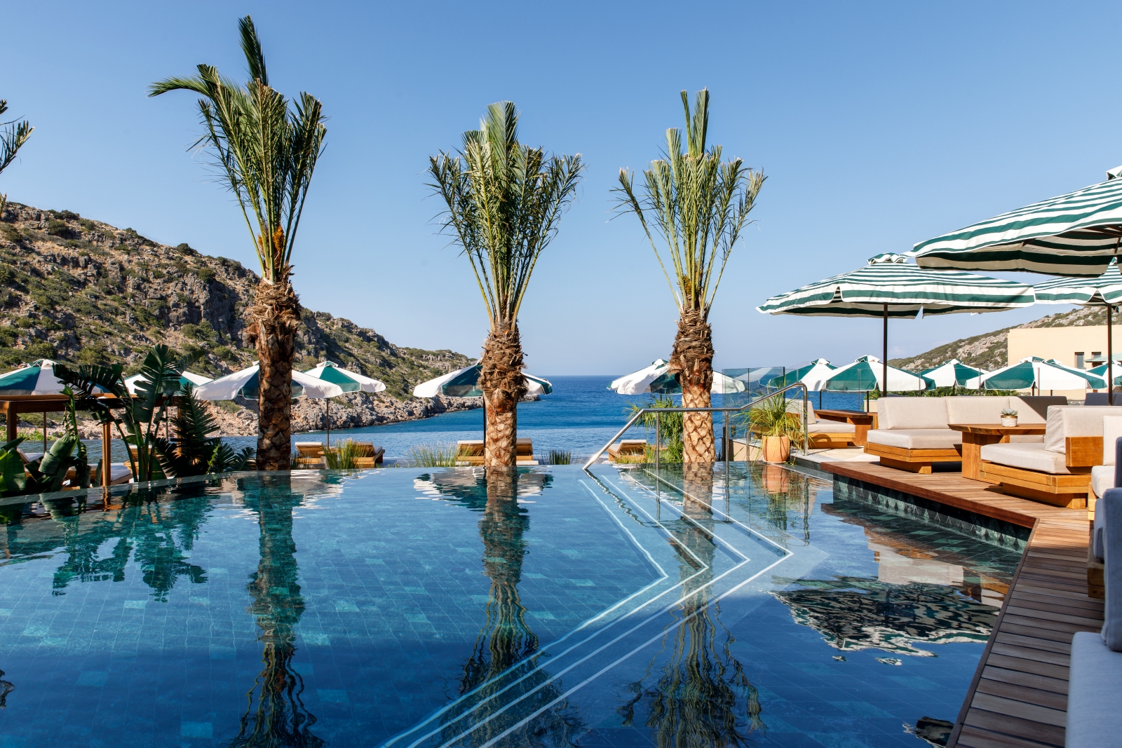 Palm tree lined adult pool with sun loungers and parasols and views over the Mediterranean Sea at luxury resort Daios Cove in Greece