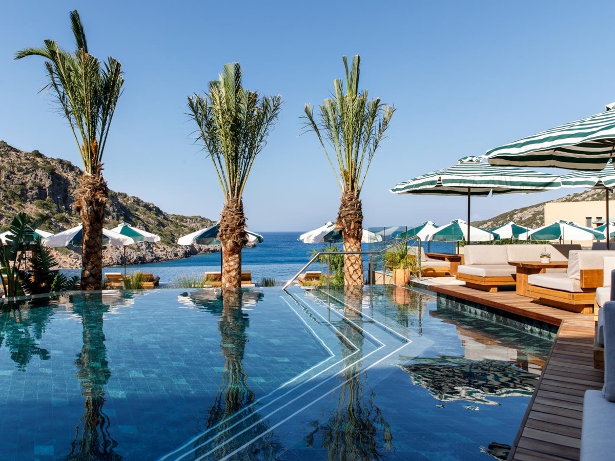 Palm tree lined adult pool with sun loungers and parasols and views over the Mediterranean Sea at luxury resort Daios Cove in Greece