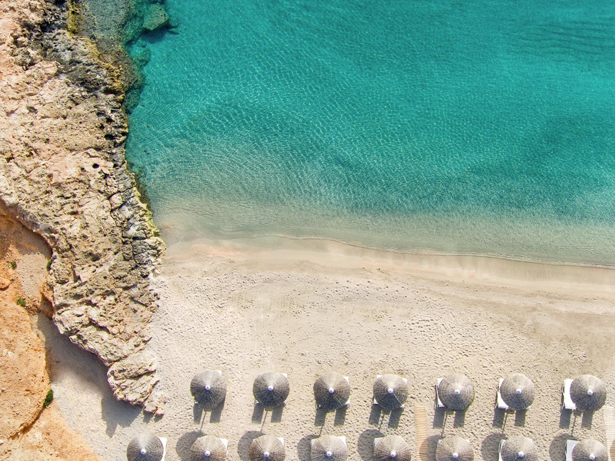 Aerial view over sun loungers and parasols on a white sand beach and the turquoise waters of the Mediterranean Sea at luxury resort Daios Cove in Greece