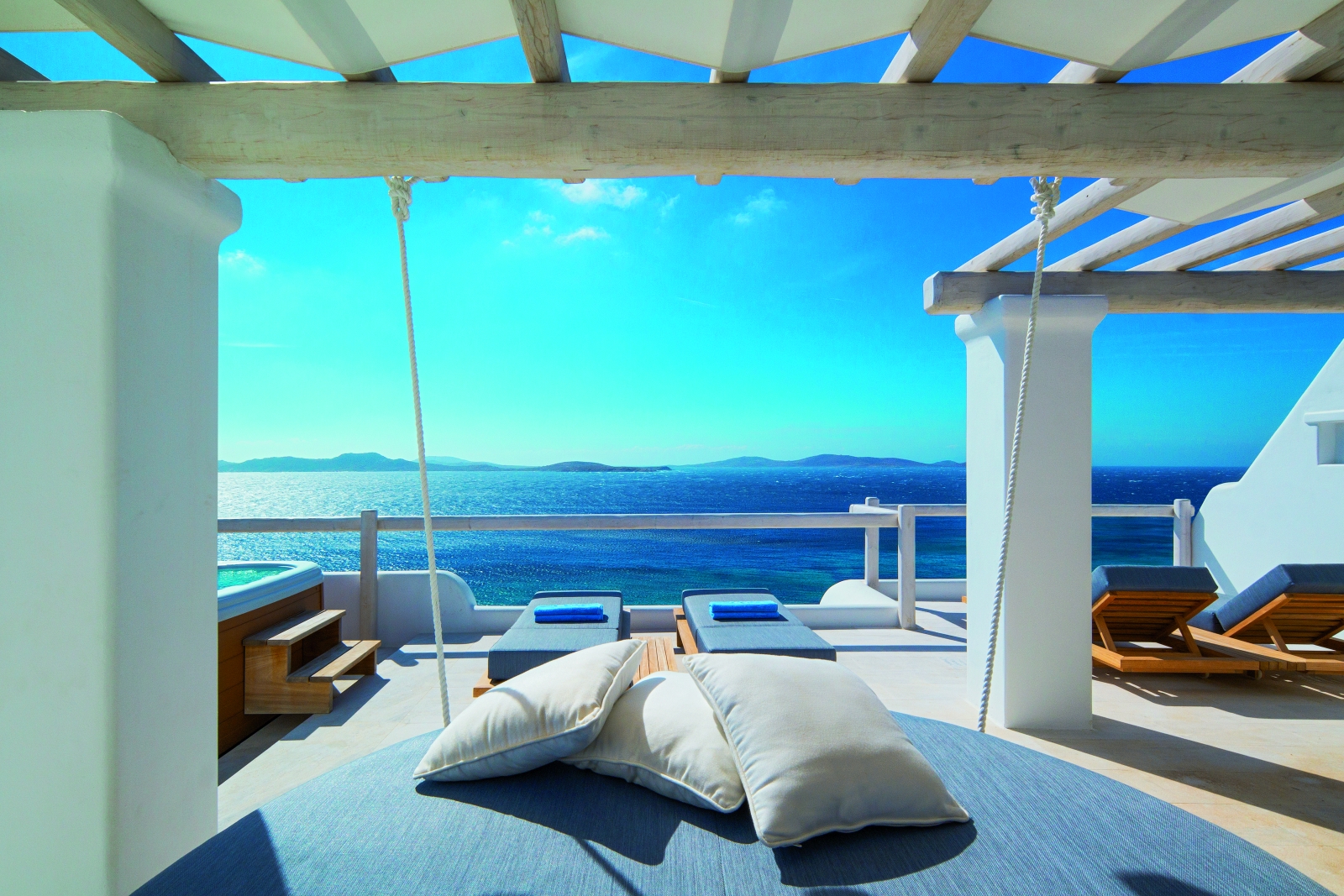 Terrace of an Executive Suite at luxury resort Mykonos Grand, Greece with sun loungers, jacuzzi and stunning views over the Aegean Sea