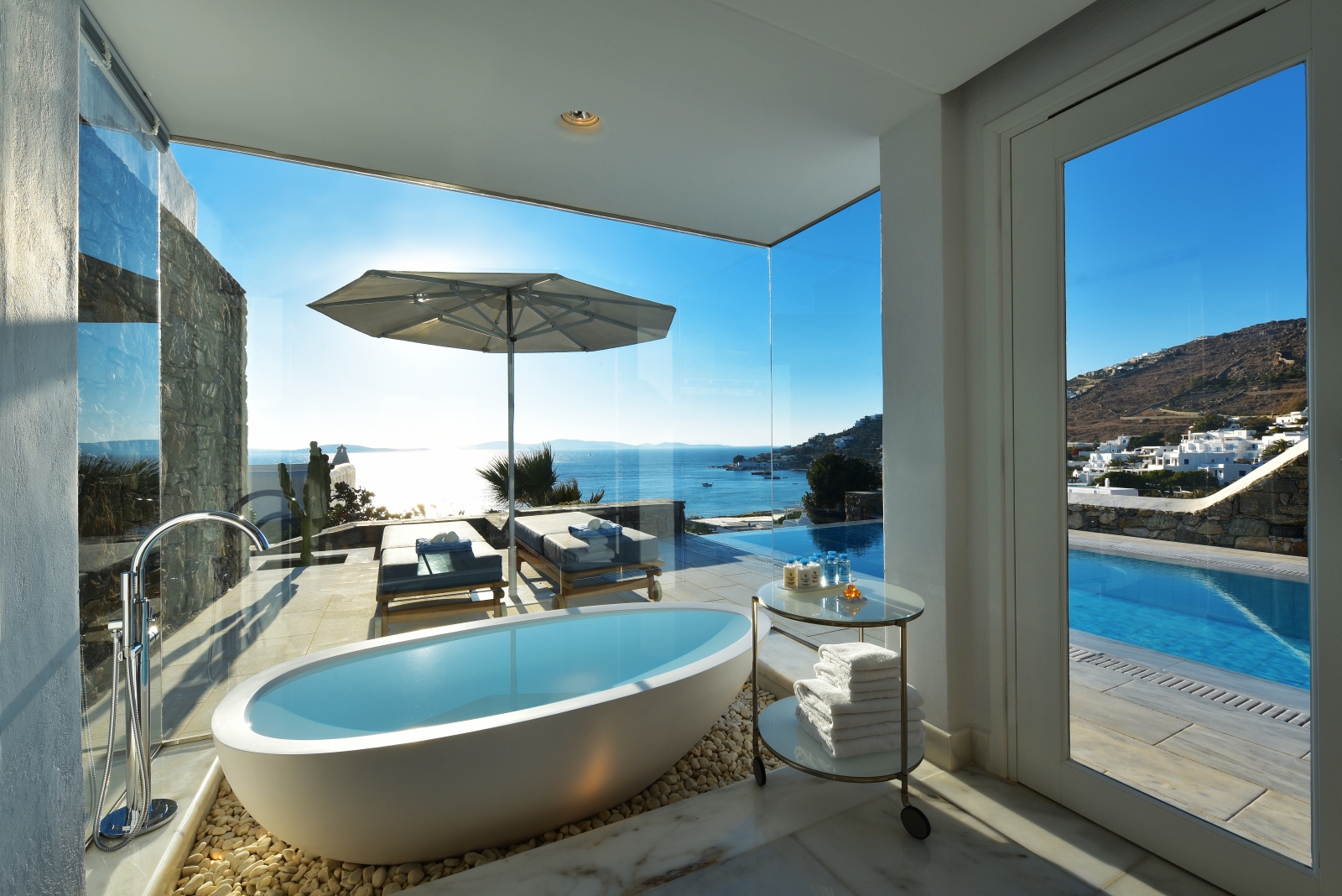 View from a freestanding bathtub in the bathroom of a Grand Suite overlooking the private pool and the Aegean Sea at luxury resort Mykonos Grand, Greece