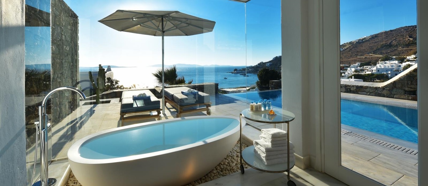 View from a freestanding bathtub in the bathroom of a Grand Suite overlooking the private pool and the Aegean Sea at luxury resort Mykonos Grand, Greece