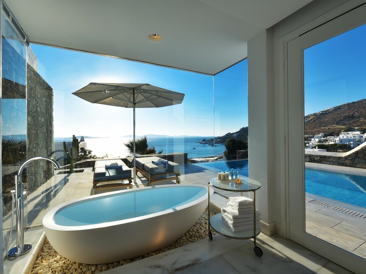 View from a freestanding bathtub in the bathroom of a Grand Suite overlooking the private pool and the Aegean Sea at luxury resort Mykonos Grand, Greece