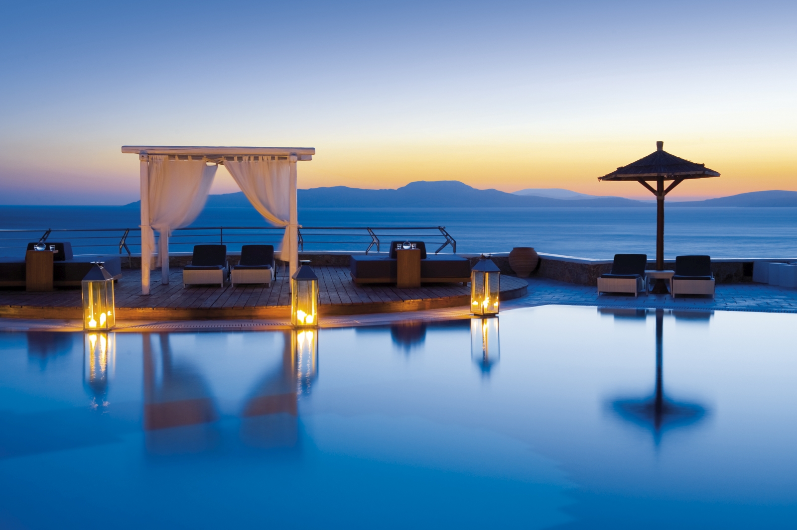 Loungers by the illuminated pool overlooking the Aegean Sea at sunset at luxury resort Mykonos Grand, Greece