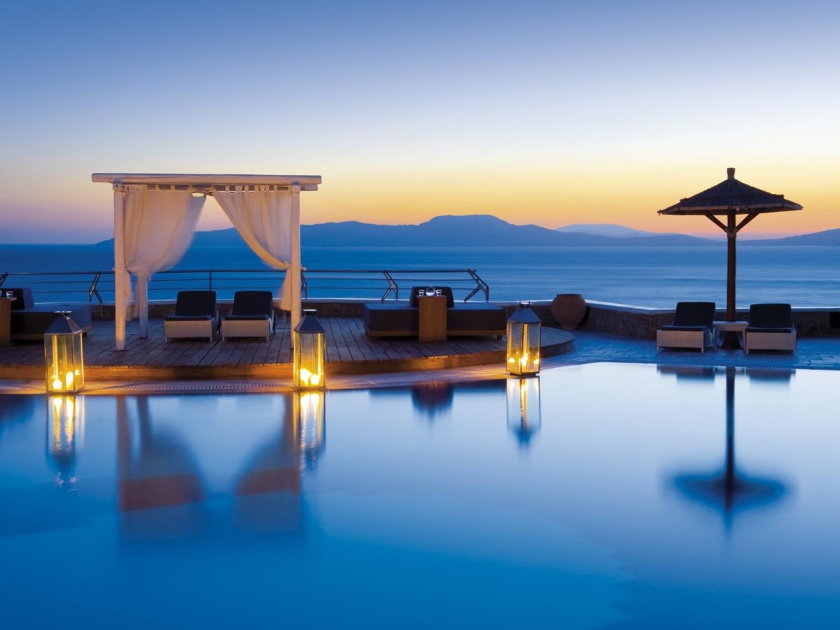 Loungers by the illuminated pool overlooking the Aegean Sea at sunset at luxury resort Mykonos Grand, Greece