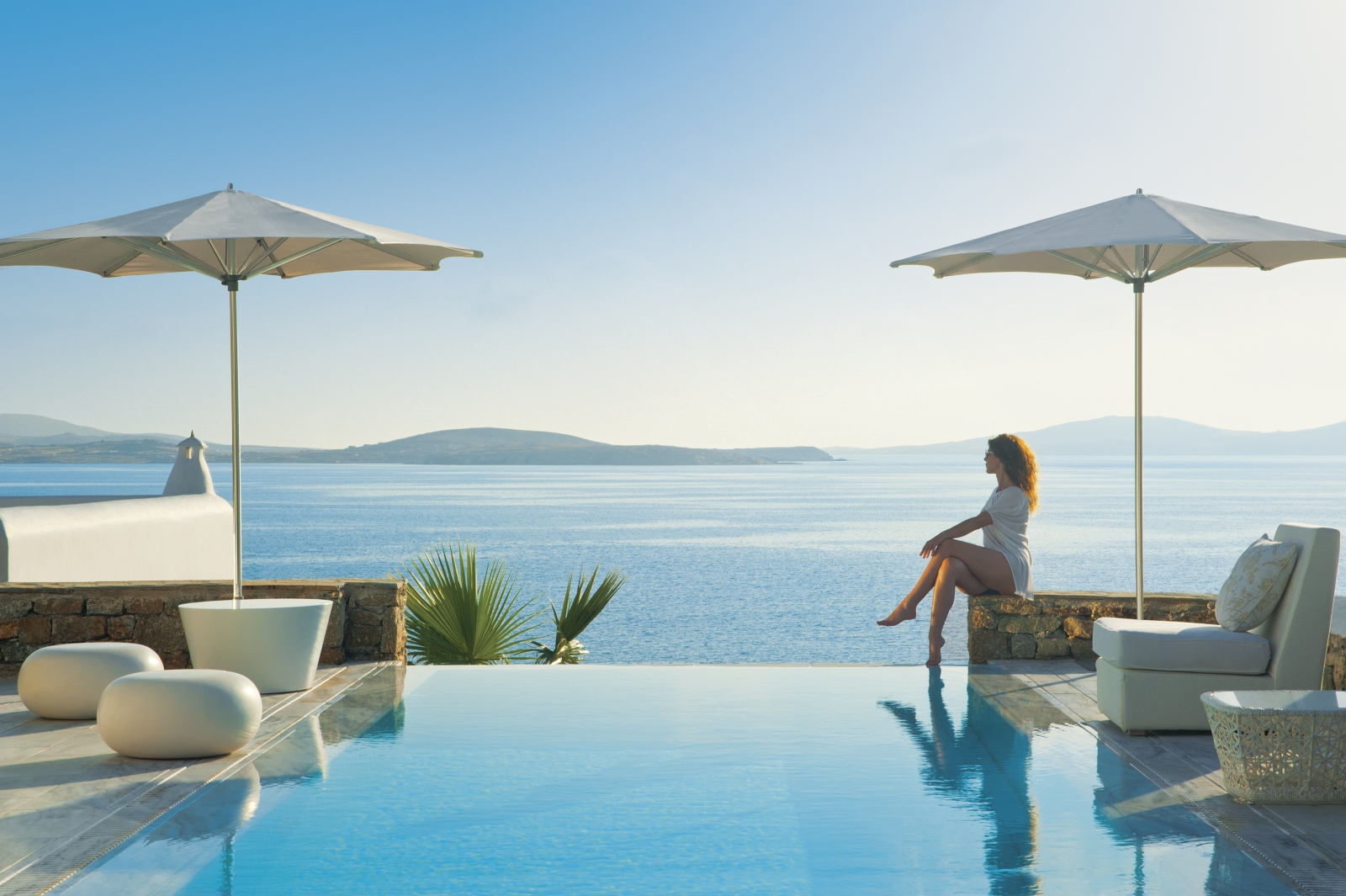 Guest sitting by the infinity pool enjoying the views over the Aegean Sea at luxury resort Mykonos Grand, Greece