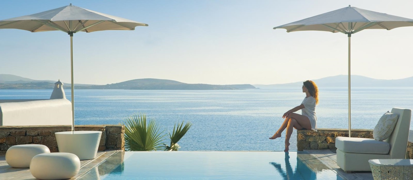 Guest sitting by the infinity pool enjoying the views over the Aegean Sea at luxury resort Mykonos Grand, Greece