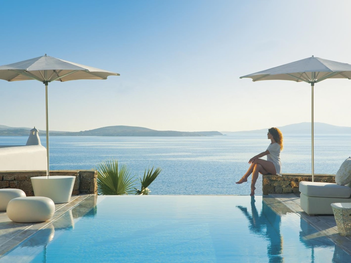 Guest sitting by the infinity pool enjoying the views over the Aegean Sea at luxury resort Mykonos Grand, Greece