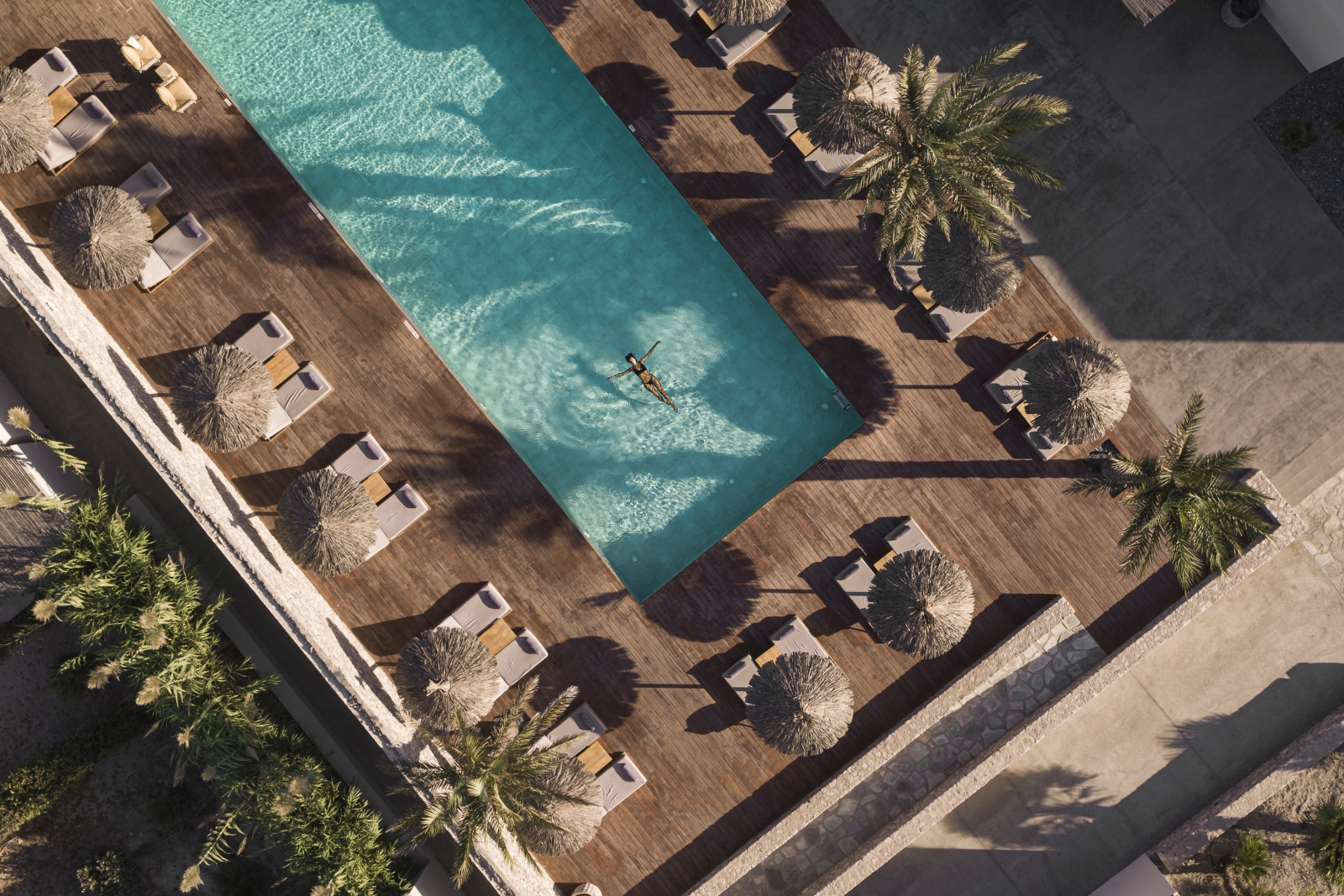 Aerial view of guests swimming in pool surrounded by loungers and parasols at luxury hotel OKU Kos in Greece