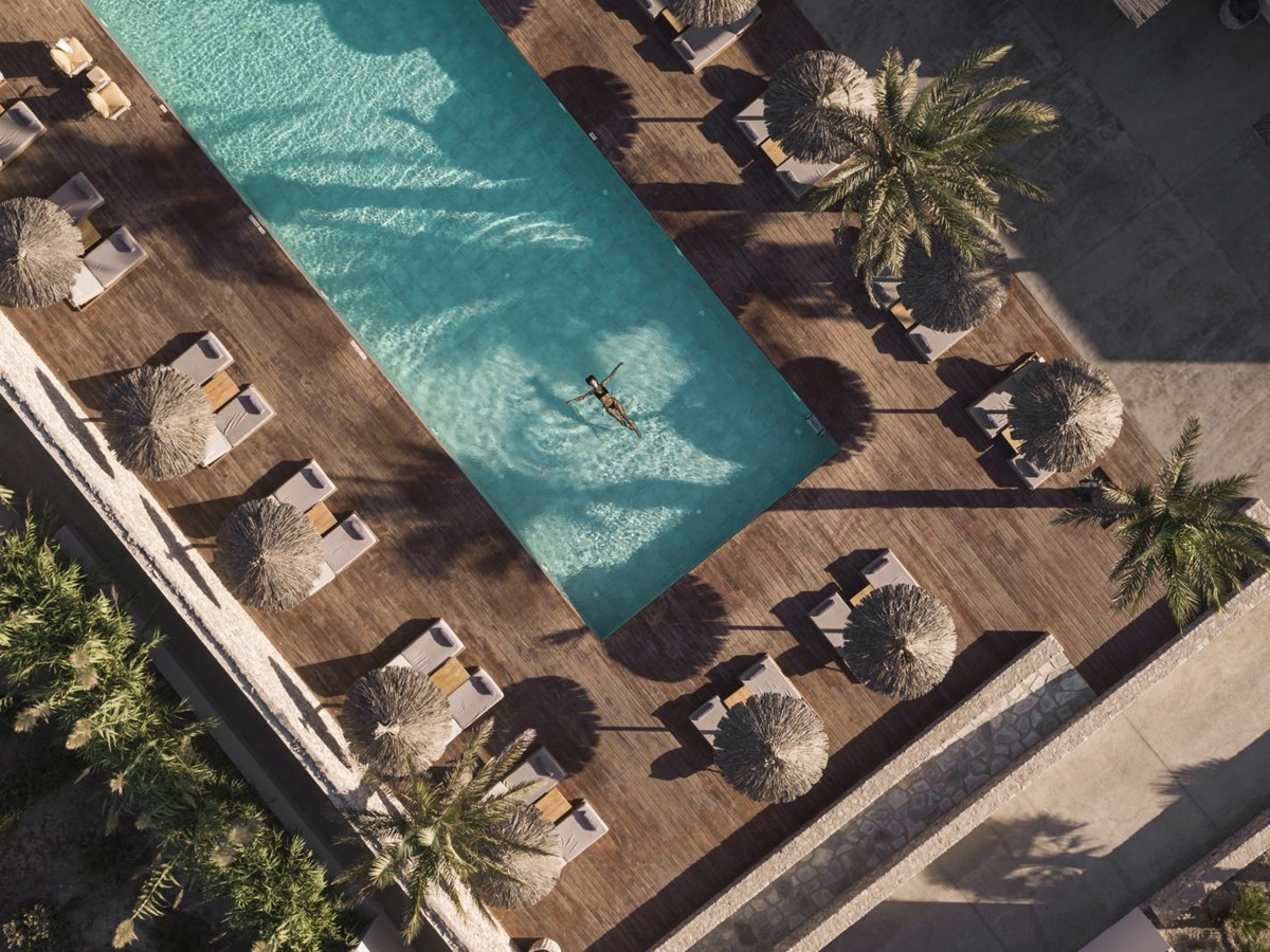 Aerial view of guests swimming in pool surrounded by loungers and parasols at luxury hotel OKU Kos in Greece