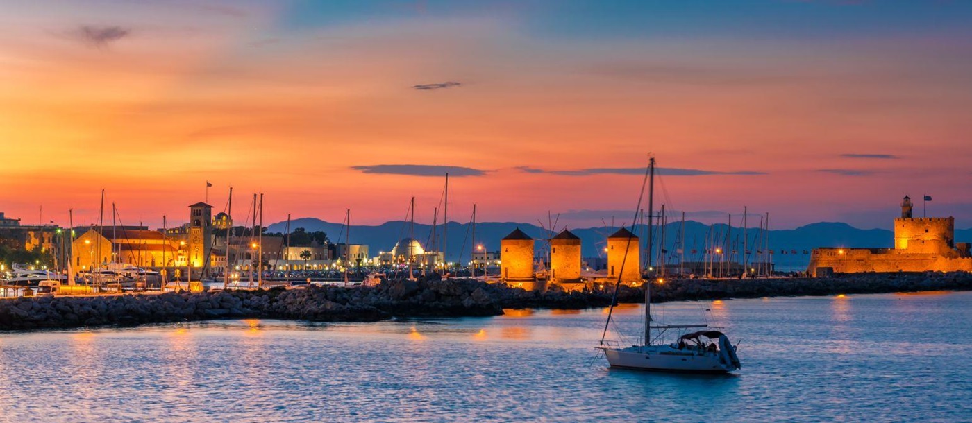 A yacht in harbour in Rhodes at sunset with illuminated windmills