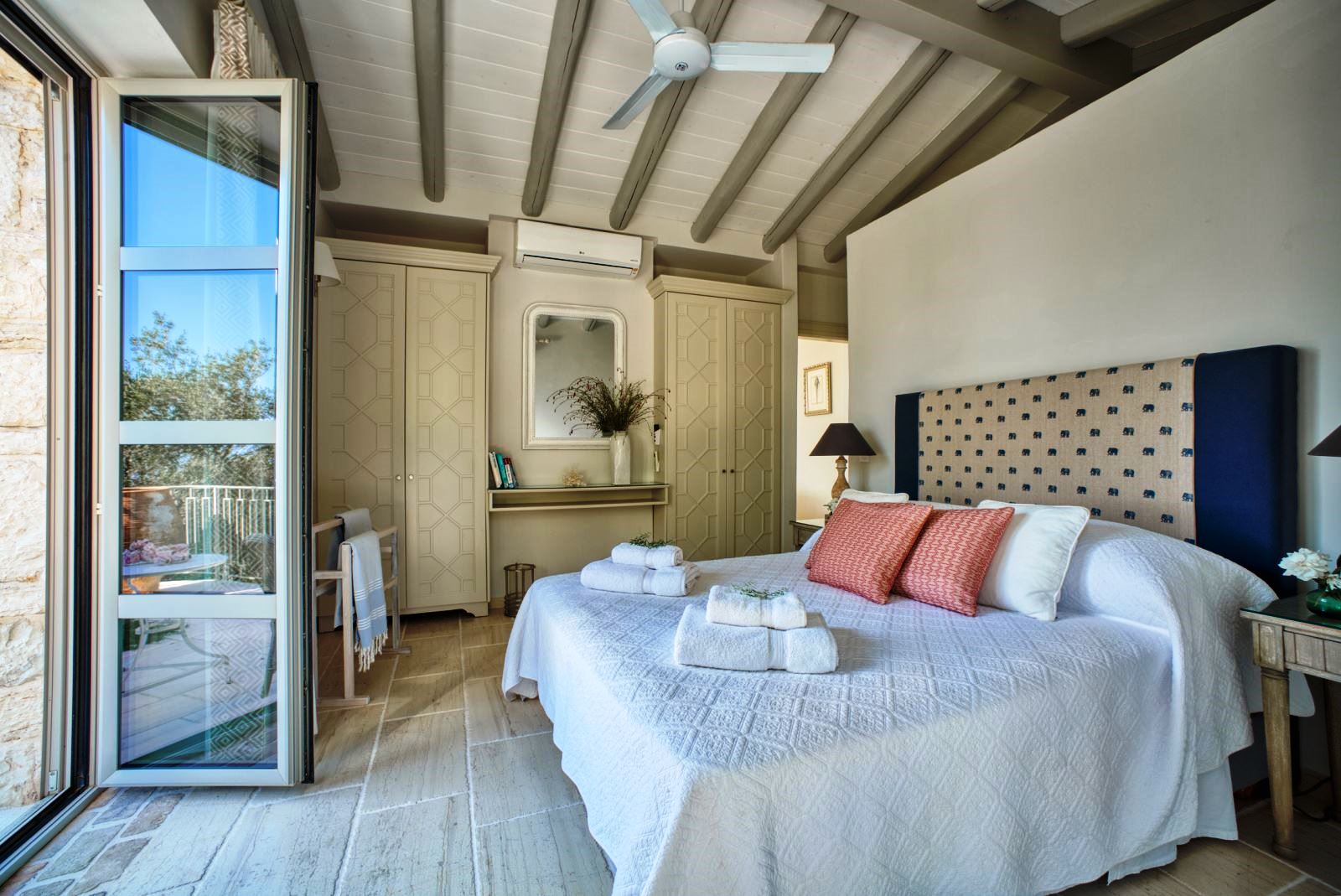 bedroom with double bed, blue patterned headboard and ceiling fan with folding glass doors at villa apraos in corfu, Greece