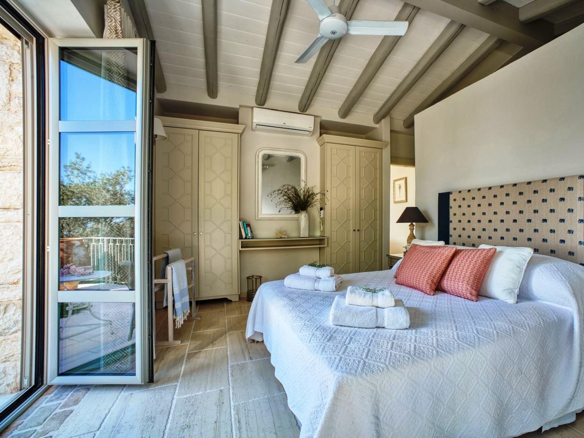 bedroom with double bed, blue patterned headboard and ceiling fan with folding glass doors at villa apraos in corfu, Greece