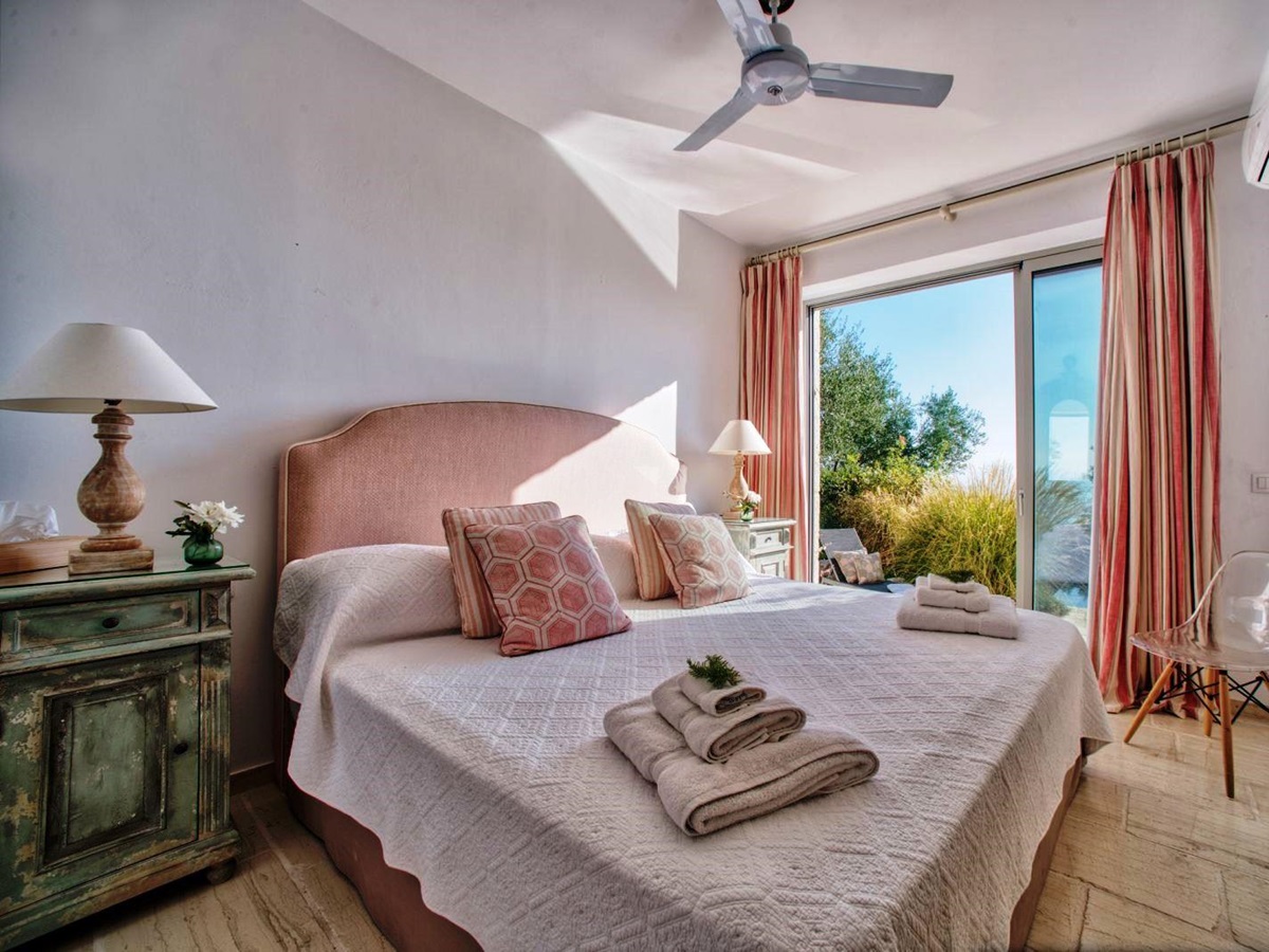 double bed with pink headboard on wooden floor and sliding glass doors onto sun terrace at villa apraos in corfu, Greece