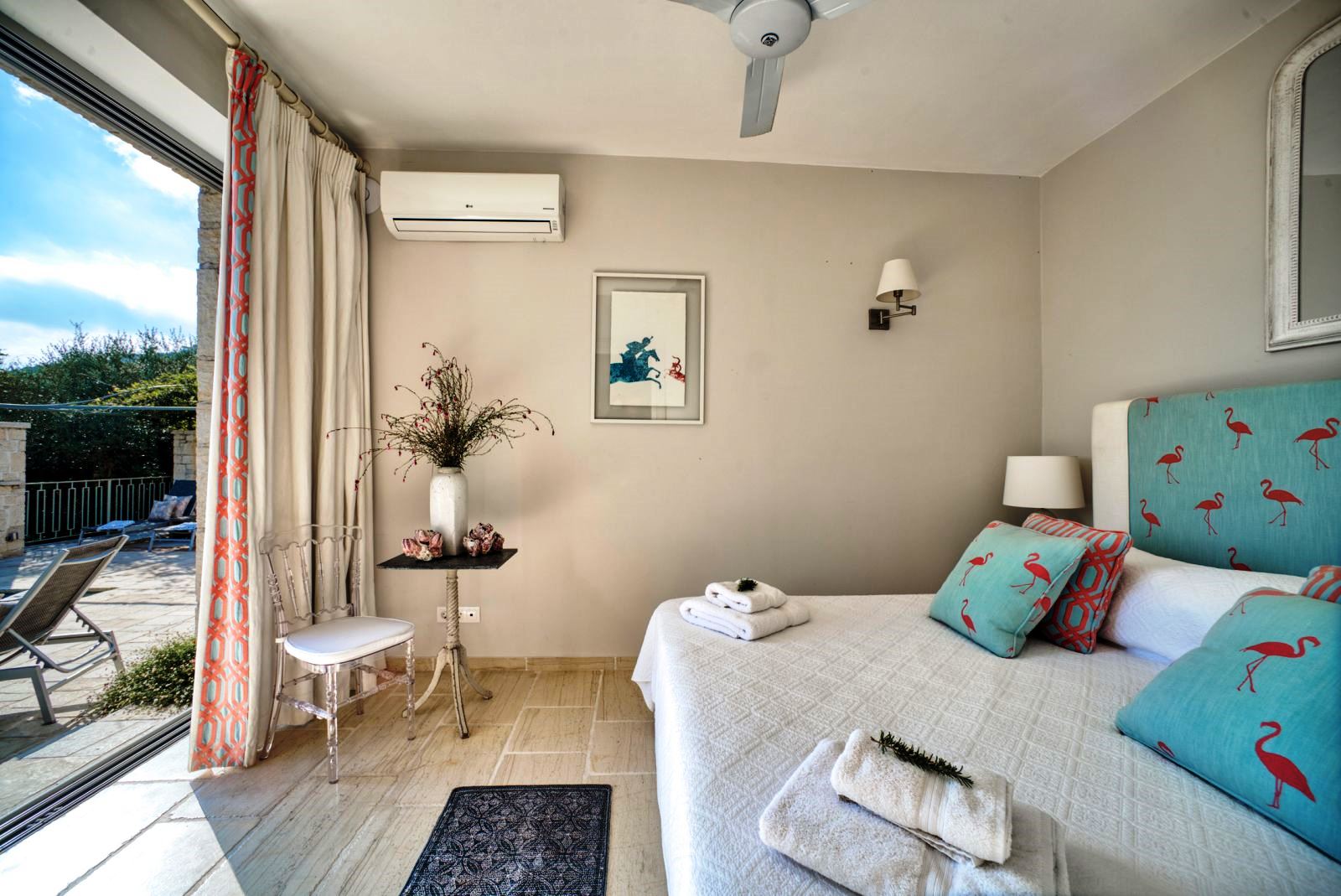 double bed with blue headboard on wooden floor and sliding glass doors onto sun terrace at villa apraos in corfu, Greece