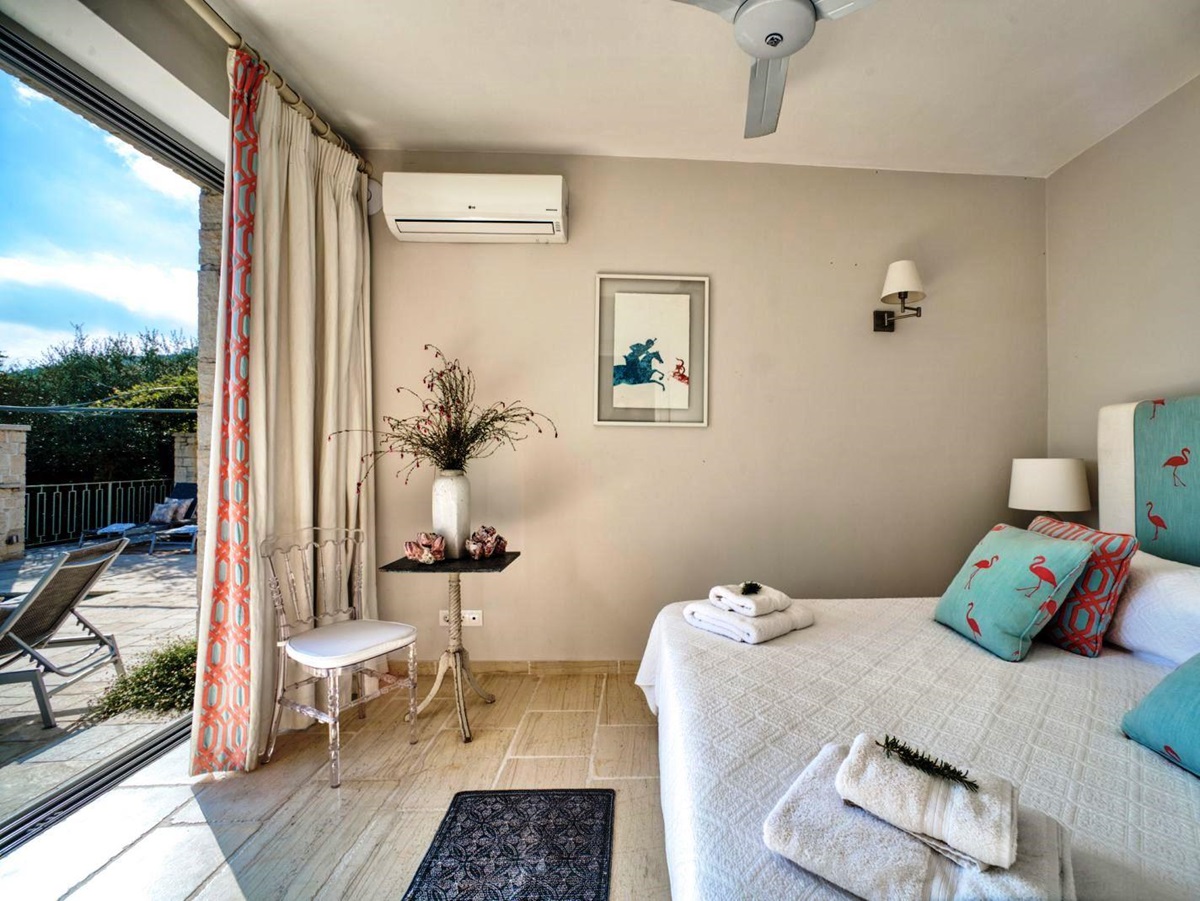 double bed with blue headboard on wooden floor and sliding glass doors onto sun terrace at villa apraos in corfu, Greece