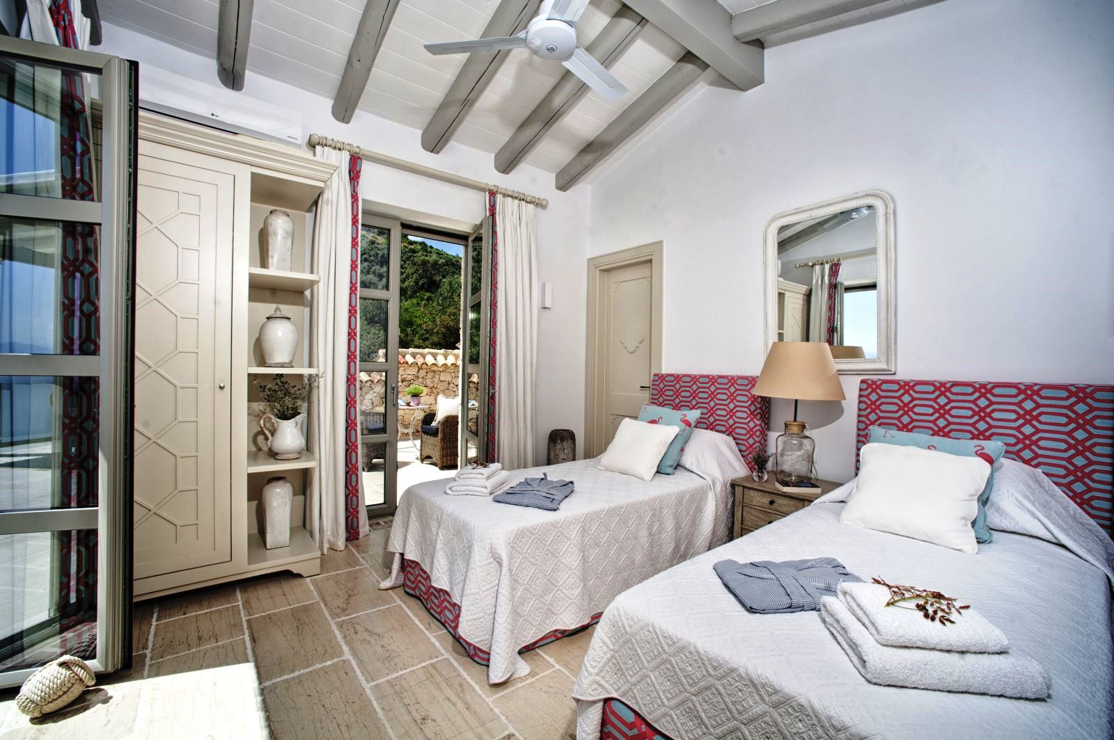 bedroom with twin beds on stone tiled floor with white cupboard and doors out to sun terrace at villa apraos in corfu, Greece