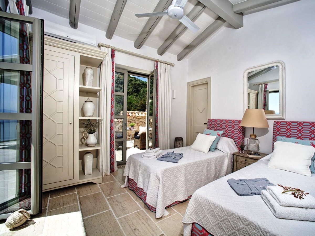 bedroom with twin beds on stone tiled floor with white cupboard and doors out to sun terrace at villa apraos in corfu, Greece