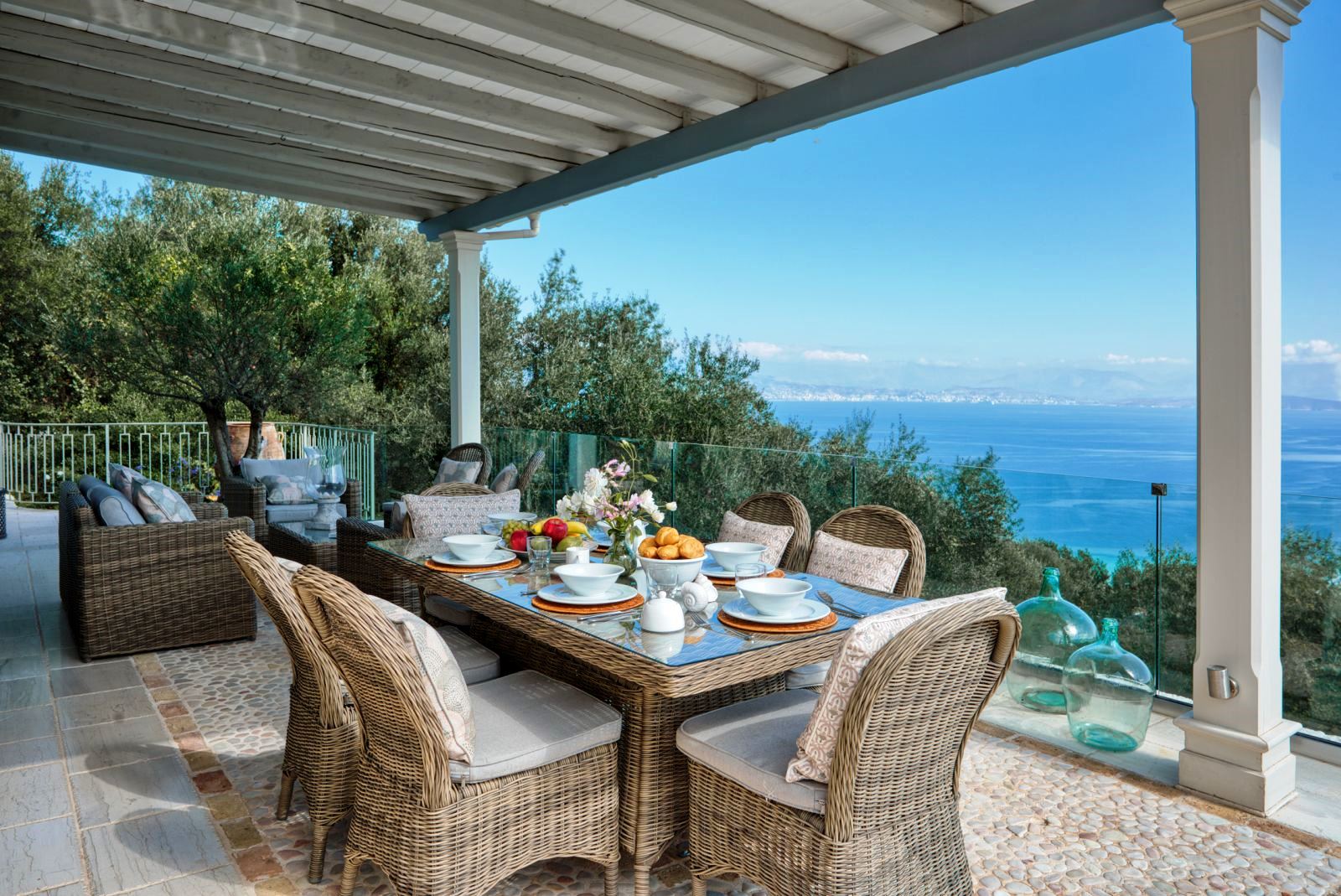 dining terrace with view of sea, wicker table set with white crockery and 6 chairs at villa apraos in corfu, Greece
