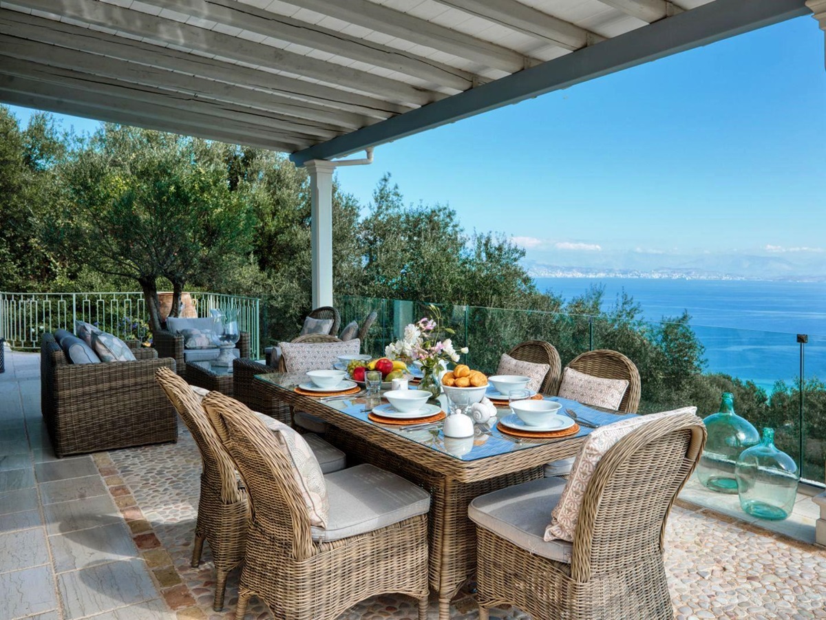 dining terrace with view of sea, wicker table set with white crockery and 6 chairs at villa apraos in corfu, Greece
