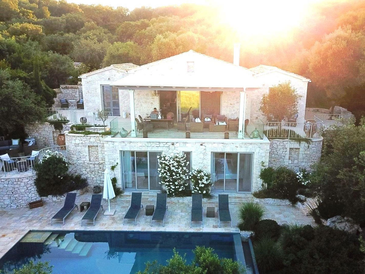 exterior view of villa apraos in corfu, Greece overlooking the pool and 6 blue sun beds with the sun behind the trees