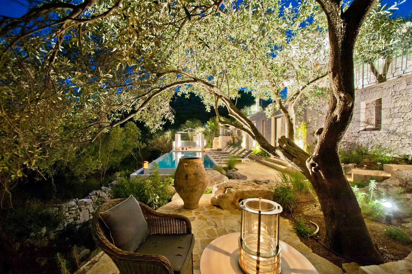 view of terrace and pool at night with chair and table under a tree lit up at villa apraos in corfu, Greece