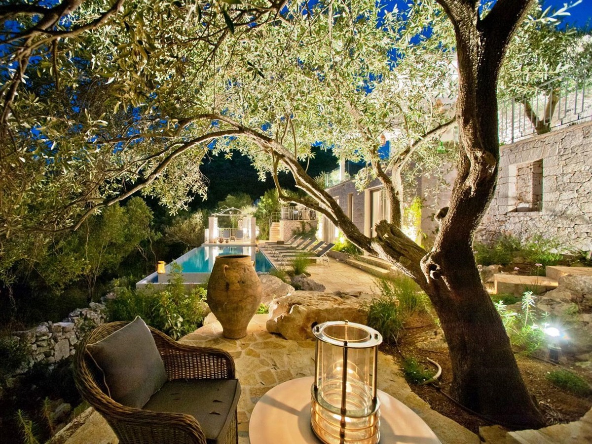 view of terrace and pool at night with chair and table under a tree lit up at villa apraos in corfu, Greece