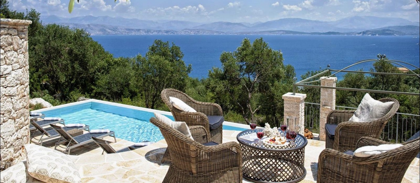 sun terrace with 4 wicker chairs and a table overlooking the pool with views of the sea at villa apraos in corfu, Greece