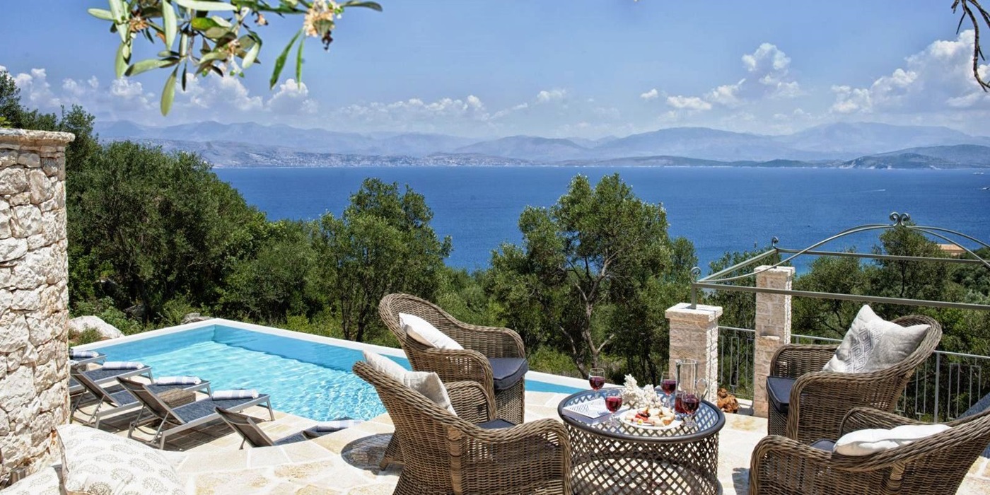 sun terrace with 4 wicker chairs and a table overlooking the pool with views of the sea at villa apraos in corfu, Greece