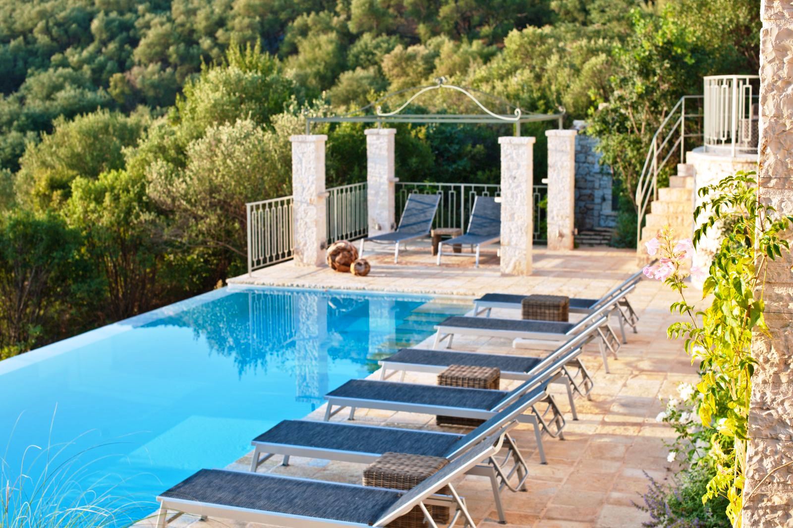 6 blue sun beds overlooking the pool with trees in the background at villa apraos in corfu, Greece