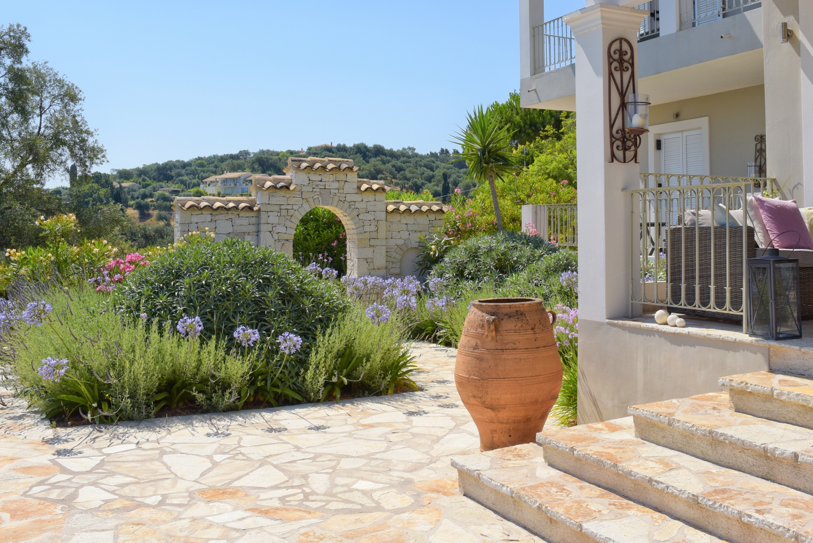 Patio with pink and purple flowers, palm tree, terracotta pot and steps to villa at Eremitis on Corfu, Greece