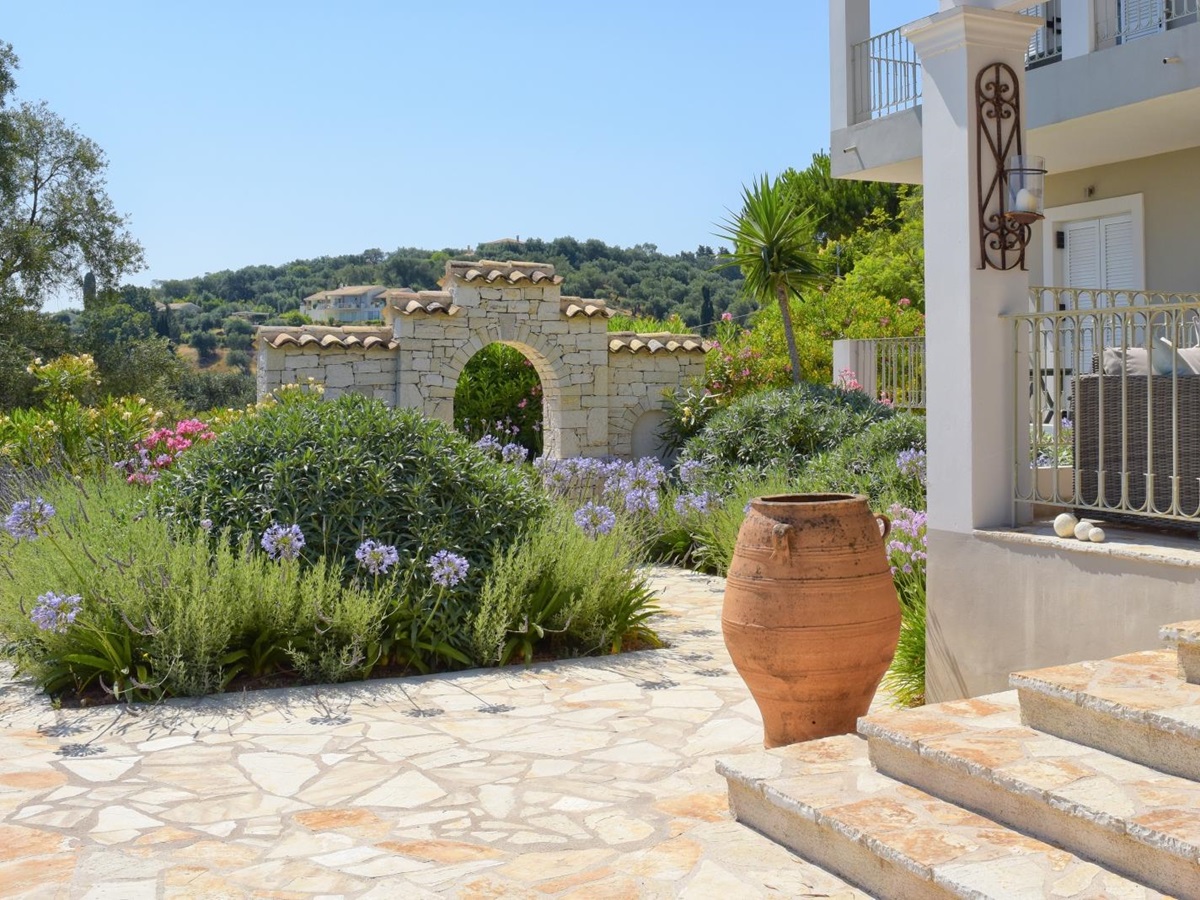 Patio with pink and purple flowers, palm tree, terracotta pot and steps to villa at Eremitis on Corfu, Greece