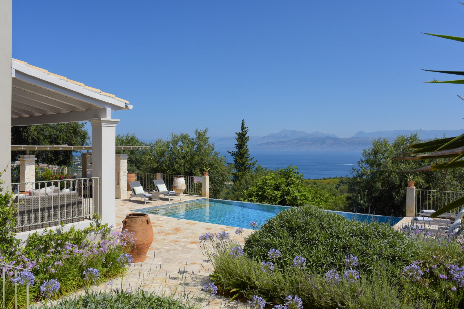 Pool area with purple flowers, terracotta pot, sun loungers and sea view at Eremitis on Corfu, Greece