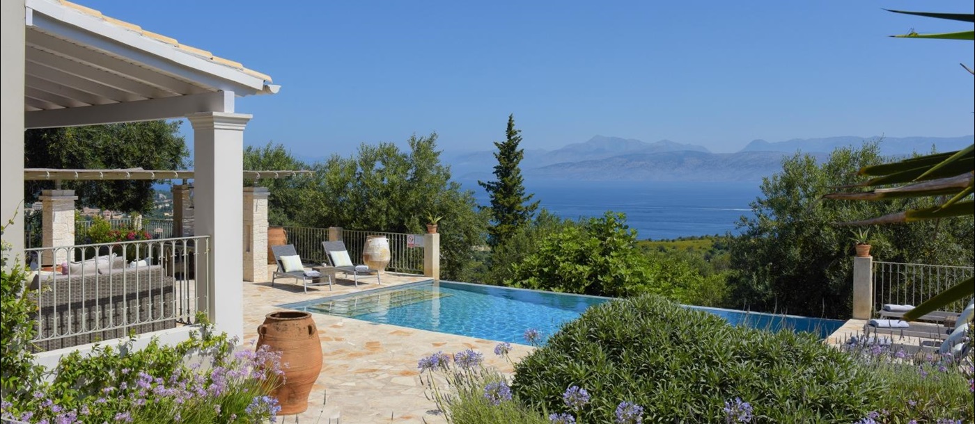 Pool area with purple flowers, terracotta pot, sun loungers and sea view at Eremitis on Corfu, Greece 