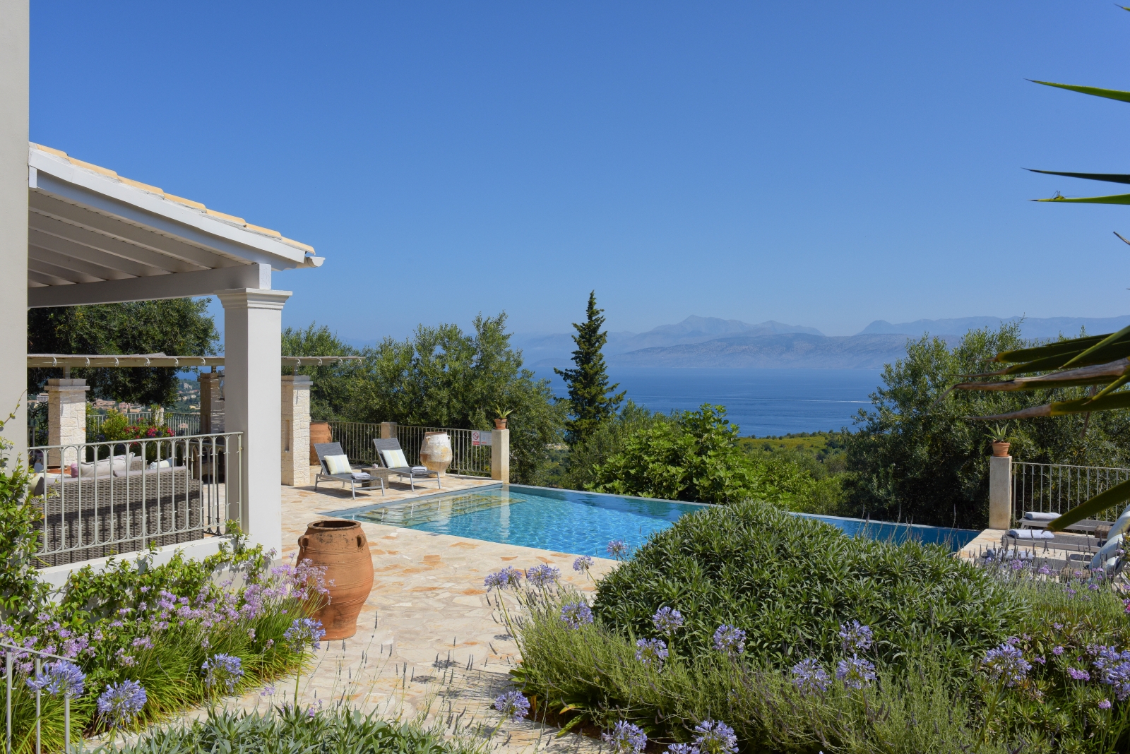 Pool area with purple flowers, terracotta pot, sun loungers and sea view at Eremitis on Corfu, Greece 
