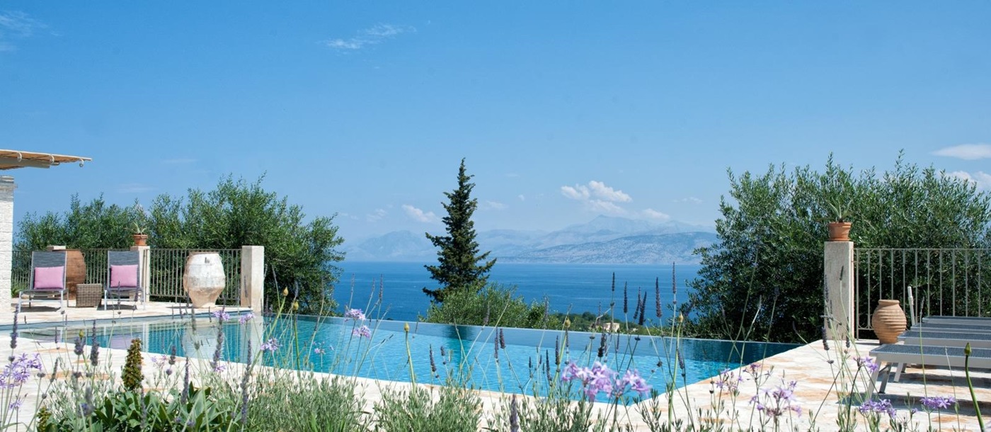 Pool area with pink flowers, sun loungers, trees and sea view at Eremitis on Corfu, Greece