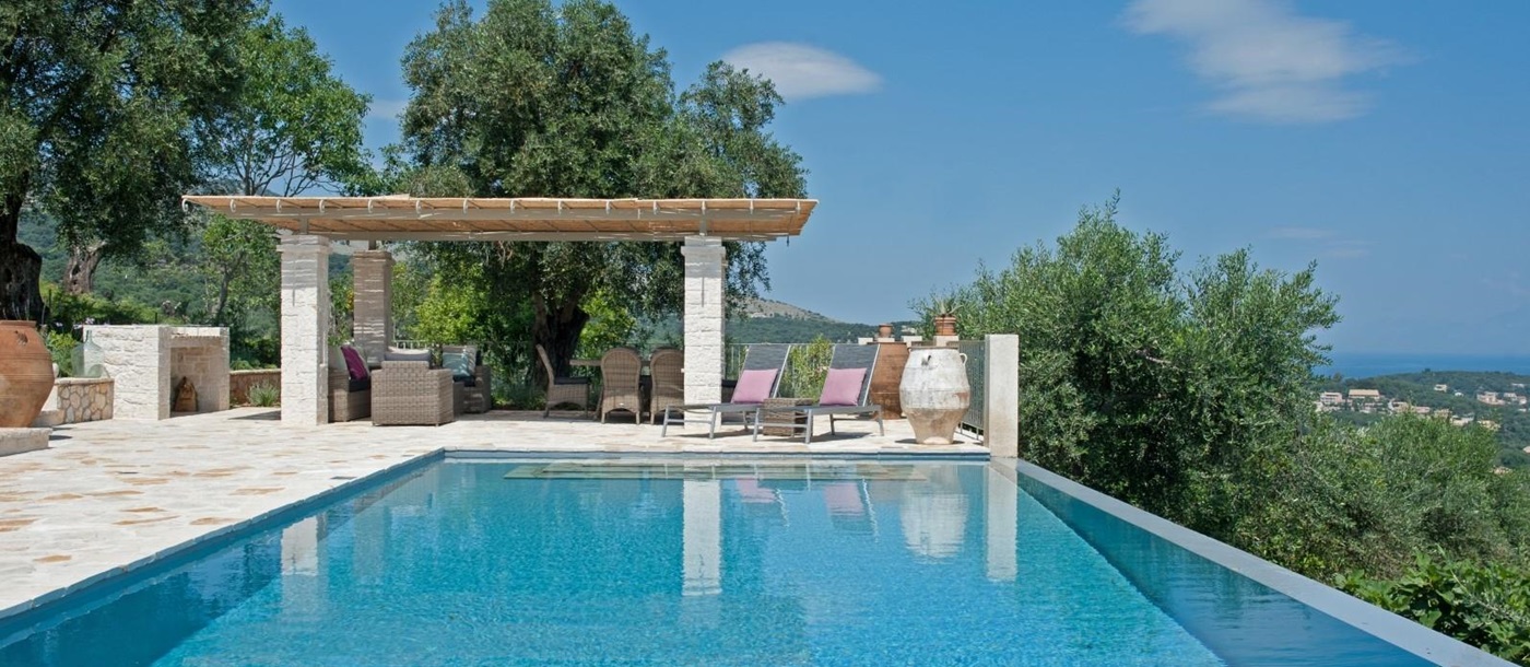 Pool area with patio, sun loungers & covered dining area with comfy chairs and table at Eremitis on Corfu, Greece