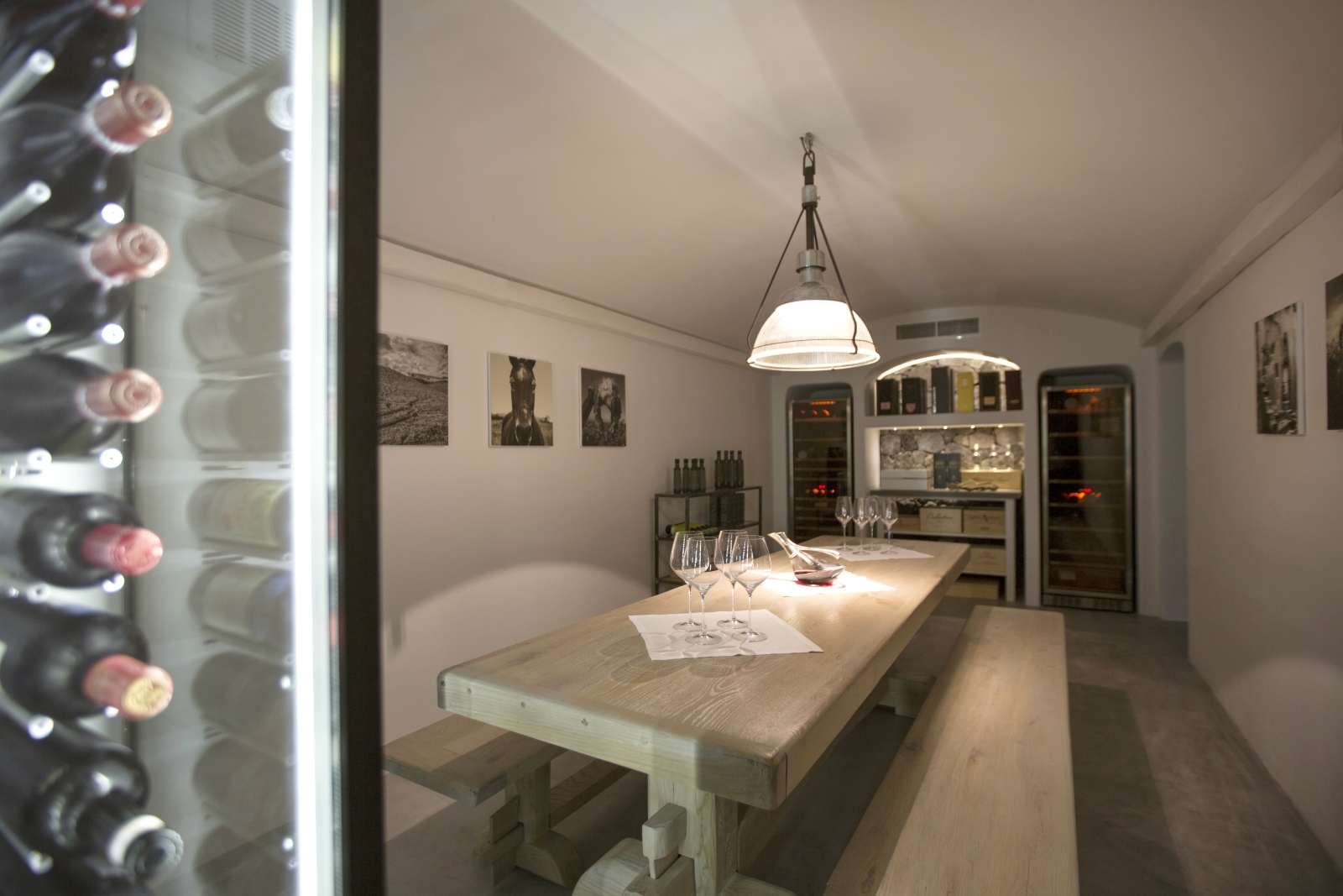 Wine cellar with dining table and bench, wine cabinets, light and pictures on walls at Erosantorini on Santorini, Greece