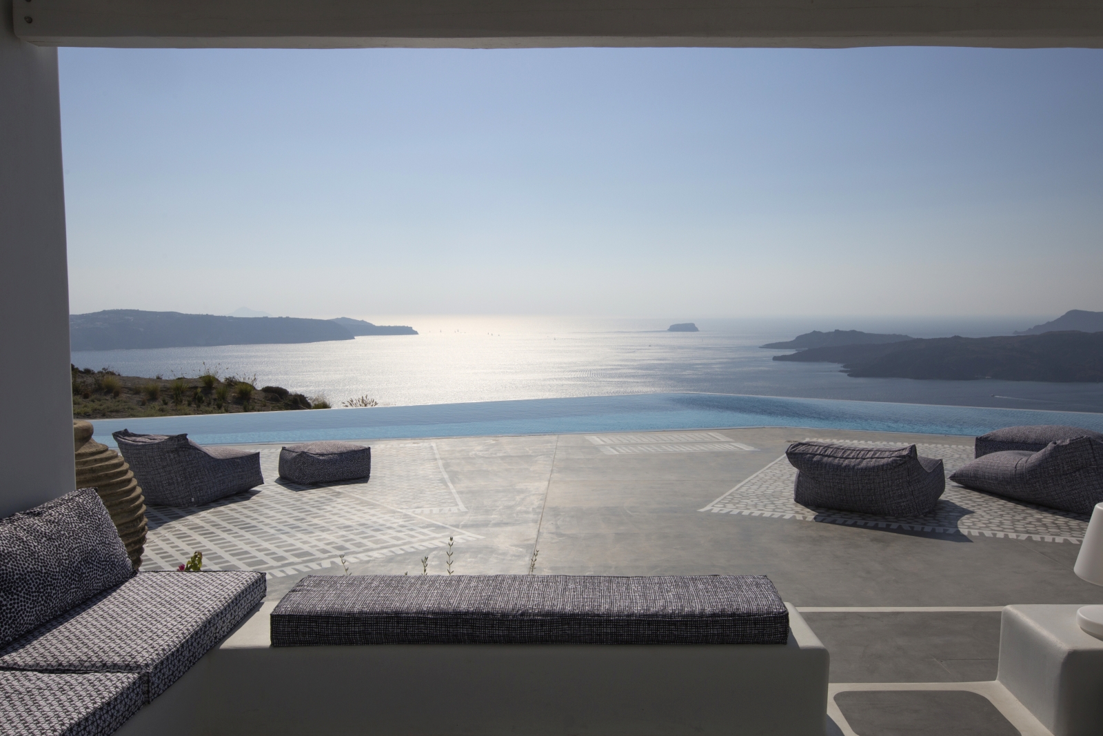 Lounge area on terrace with sofa, bench, bean bags and view of infinity pool and sea at Erosantorini on Santorini, Greece