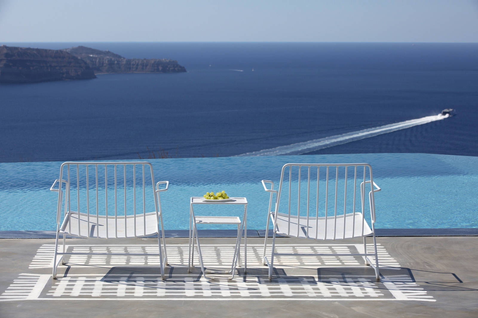 Chairs and coffee next to infinity pool on terrace with sea view at Erosantorini on Santorini, Greece