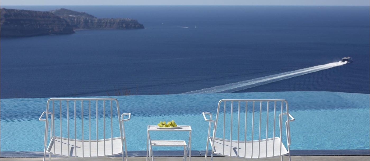 Chairs and coffee next to infinity pool on terrace with sea view at Erosantorini on Santorini, Greece