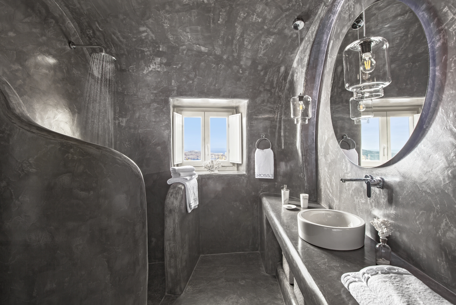 Bathroom with grey walls, sink, mirror, hanging lights, shower and window at Erossea on Santorini, Greece