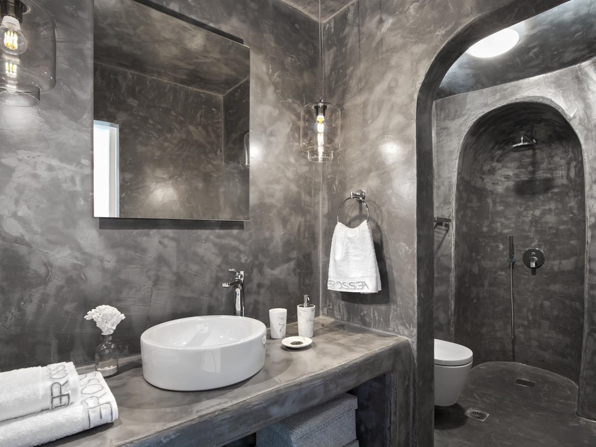 Bathroom with grey walls, sink, hanging lights, mirror, toilet and shower at Erossea on Santorini, Greece