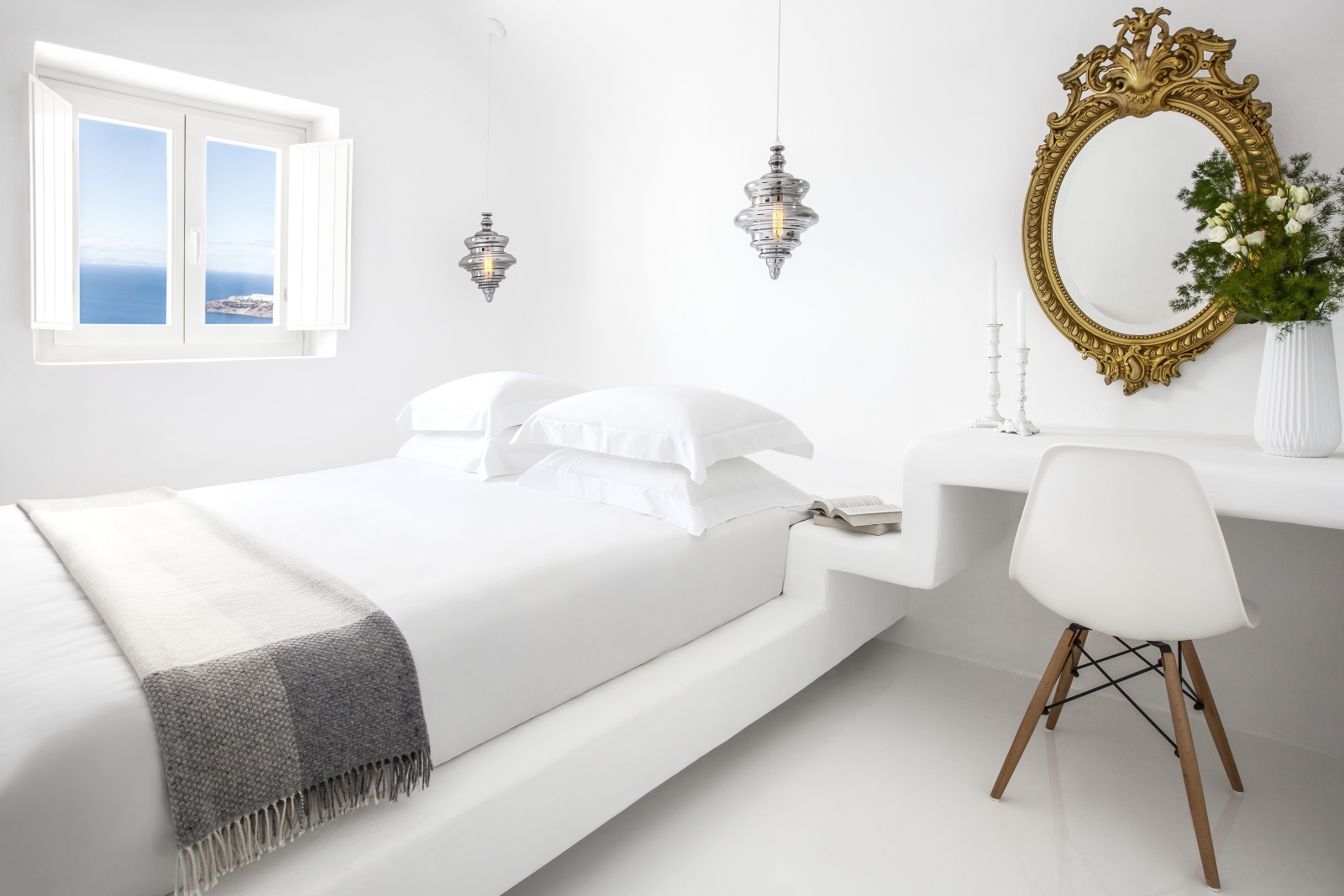 Bedroom with double bed, desk, chair, candles, plant, mirror, hanging lights and window at Erossea on Santorini, Greece