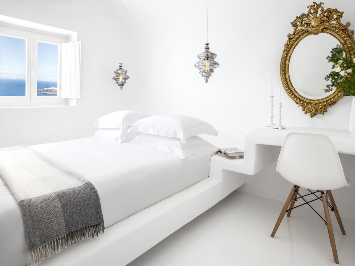 Bedroom with double bed, desk, chair, candles, plant, mirror, hanging lights and window at Erossea on Santorini, Greece