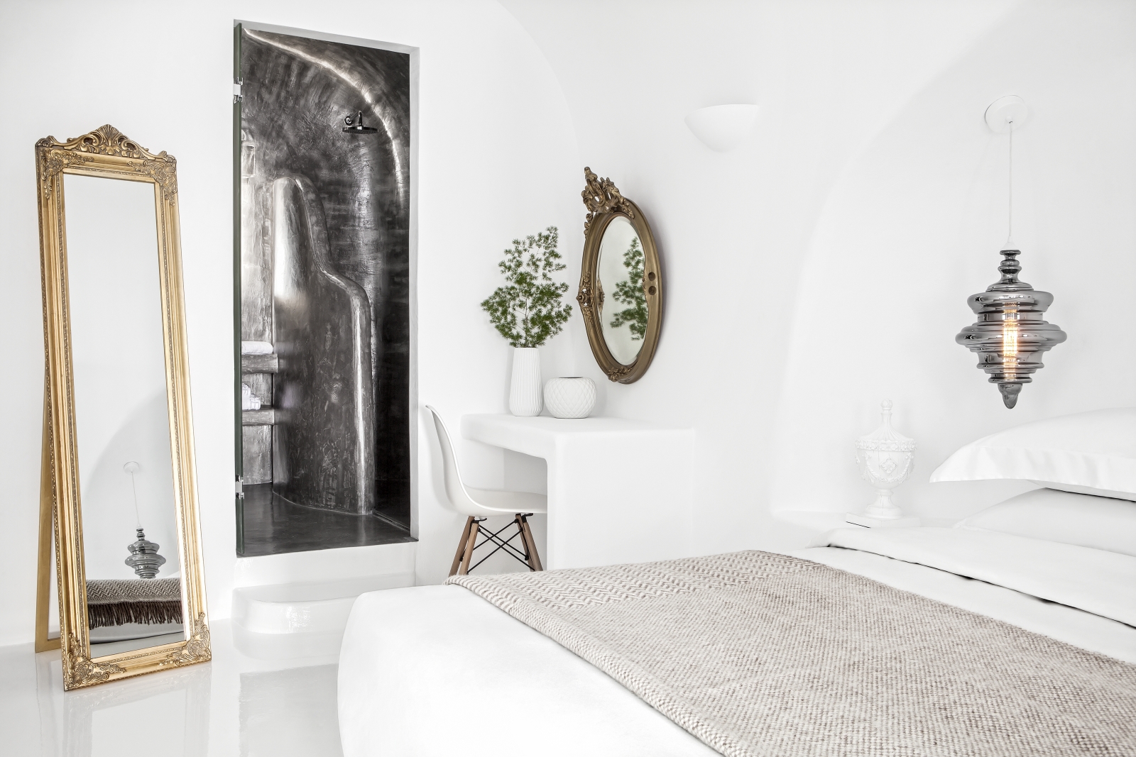 Bedroom with double bed, hanging light, desk, chair, mirrors & plant at Erossea on Santorini, Greece