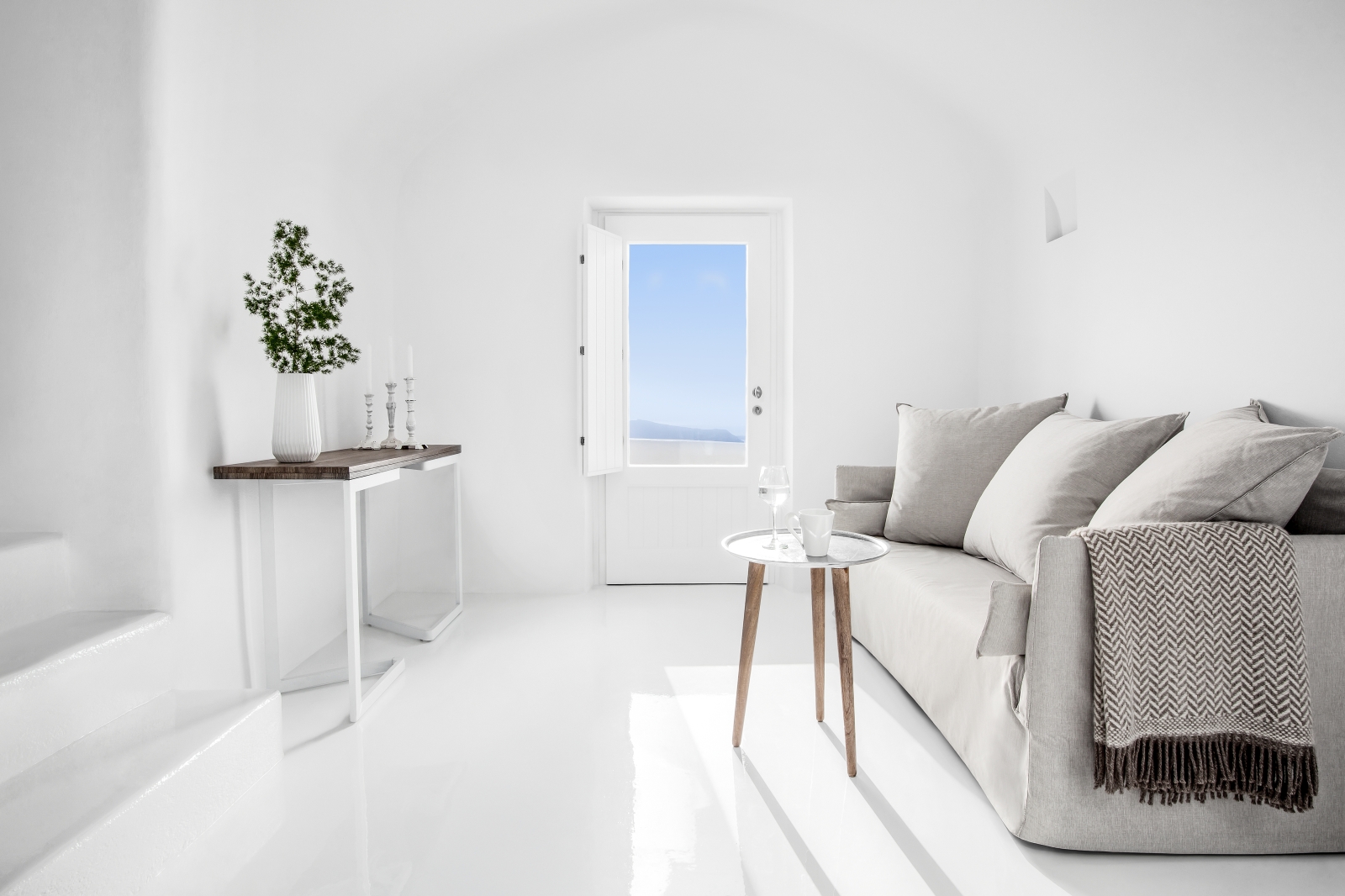 Living room with sofa, tables, plant, candle and door at Erossea on Santorini, Greece