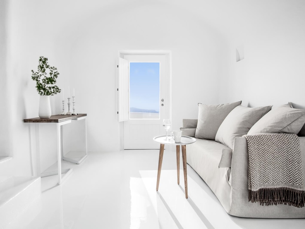 Living room with sofa, tables, plant, candle and door at Erossea on Santorini, Greece
