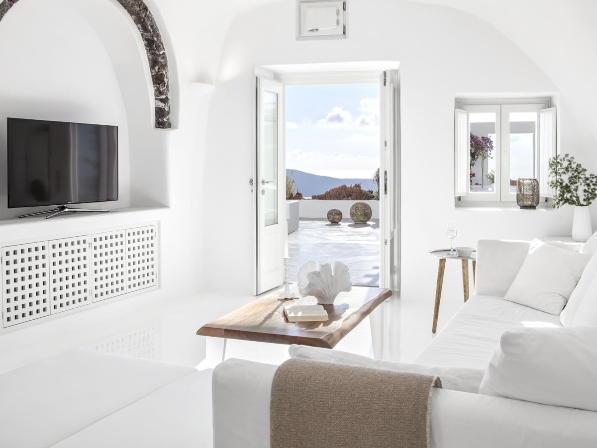 Living room with sofa, coffee table, TV, plant and doors to balcony at Erossea on Santorini, Greece