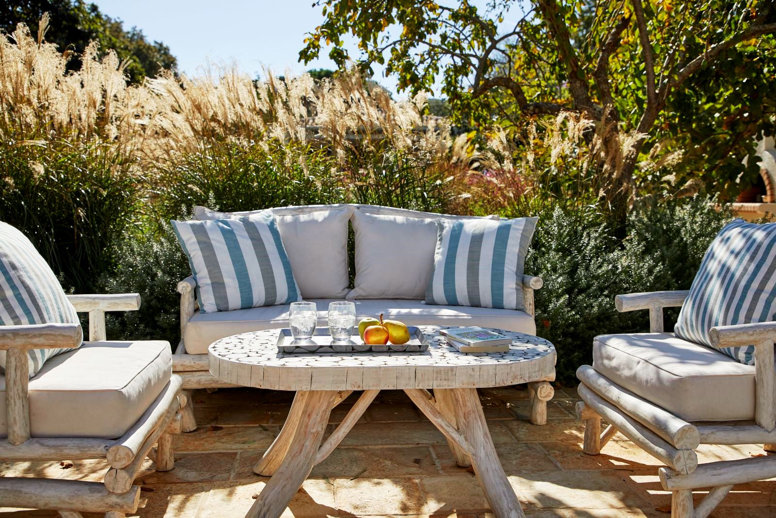 outdoor wooden table and chairs wth blue and white cushions on terrace at kogevina beach villa in corfu, greece